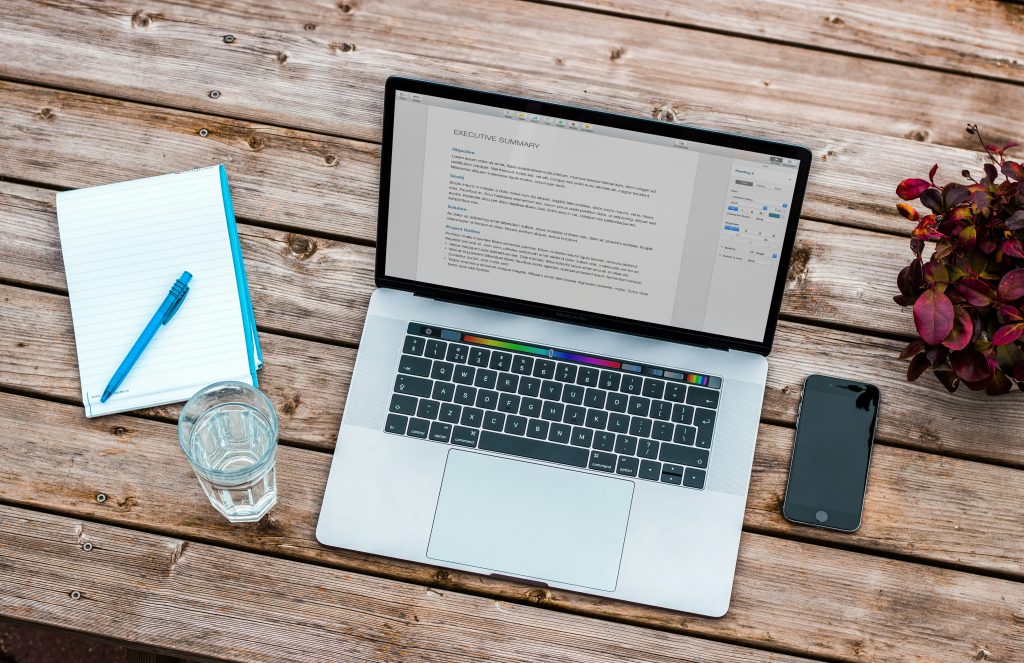 An open laptop on a table displays an outline of an Executive Summary.