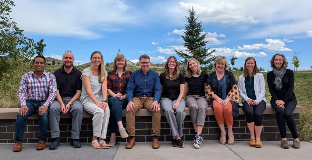 The L Pro team poses for a group photo, seated with a beautiful Colorado backdrop, all smiling.